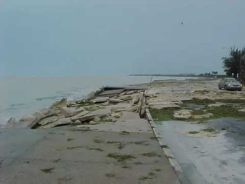 Broken concrete slabs along the top of a seawall on the Key West shoreline after a storm